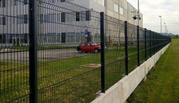 3D PVC coated fence is fixed upon concrete around a white building.