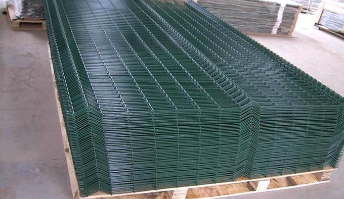 Green 3D fence panels are packed on the top of each other in a wooden pallet.