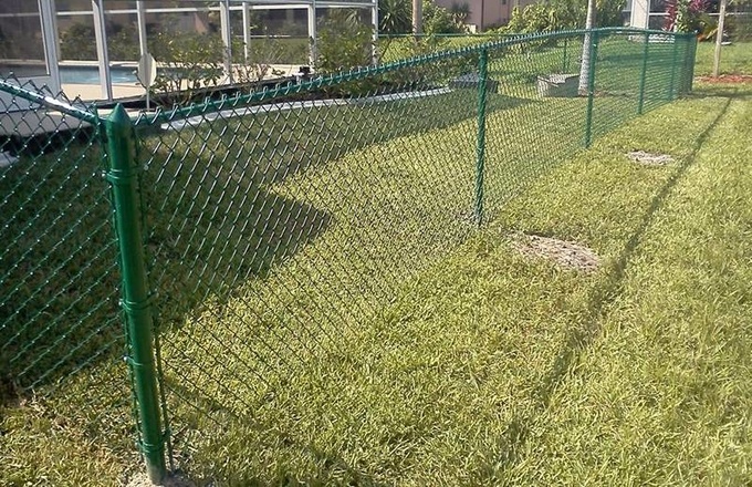 Green vinyl-coated residential chain link fence matching with the grass.